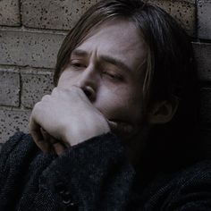 a man leaning against a brick wall with his hand on his face