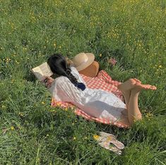 a woman laying in the grass reading a book with her legs crossed and hat on her head