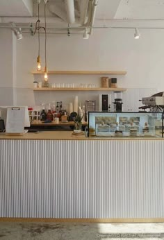 an empty restaurant with white walls and wooden counter tops, along with hanging lights above the bar