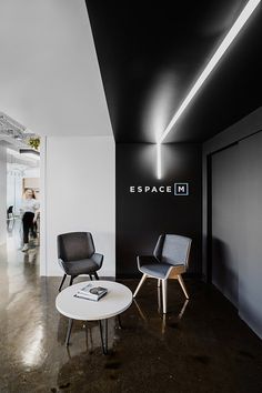 two chairs and a table in a room with black walls, white floors and an espace m logo on the wall