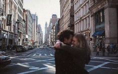 a man and woman are walking down the street in new york city, with tall buildings behind them