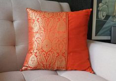 an orange and gold pillow sitting on top of a white couch next to a framed photograph