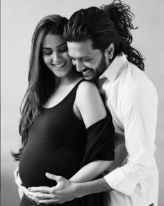 a pregnant couple cuddles while posing for a black and white photo with their belly wrapped around each other