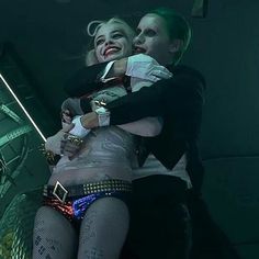 two people dressed as the joker and harley hugging each other in front of a mirror