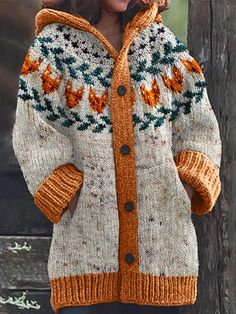 a woman wearing an orange and white knitted jacket with flowers on the front, standing next to a wooden fence