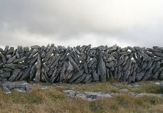 a stone wall with grass and rocks in the foreground, on a cloudy day