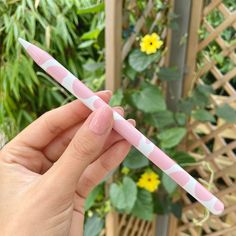 a person holding a pink and white pen in front of a plant with yellow flowers