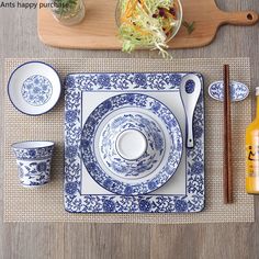 a place setting with blue and white plates, chopsticks, orange juice and salad