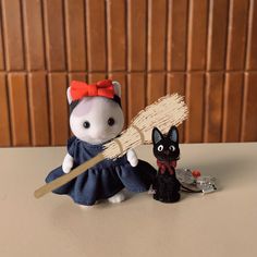 a small white mouse with a red bow holding a broom and a black cat figurine