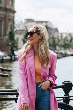 a woman standing on the side of a boat wearing sunglasses and a pink blazer