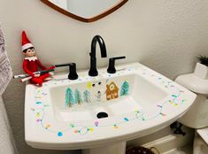 an elf sitting on the edge of a bathroom sink next to a christmas themed mirror