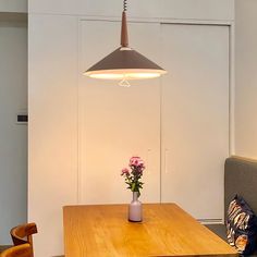 a wooden table with flowers in a vase on it and a light hanging from the ceiling