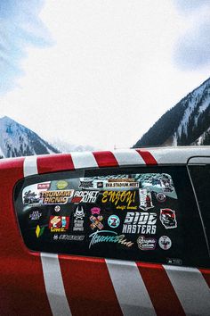 a red car with stickers on it parked in front of snow covered mountain tops