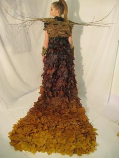 a woman in a long dress made out of leaves and branches is standing on a white background