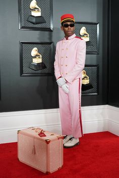 a man in a pink suit and hat standing next to an open suitcase on a red carpet