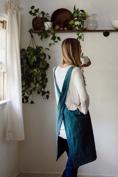 a woman standing in front of a wall with potted plants on top of it