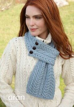 a woman with long red hair wearing a blue scarf and white sweater standing in the grass