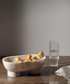 a marble bowl with lemons in it and a glass on the table next to it