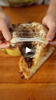 a person holding a slice of pizza on top of a wooden table