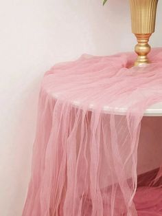 a pink table with a gold vase on top and a rose in the corner next to it