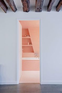 an open door leading to a bathroom with pink tiles and wood beams on the ceiling