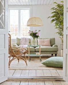 an open door leading to a living room with white walls and wood flooring, green furniture and potted plants