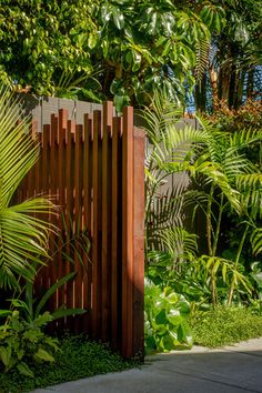 a wooden gate surrounded by lush green plants and trees on the side of a road