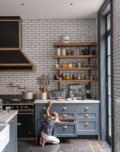 a woman kneeling on the floor in front of a stove top oven next to a counter