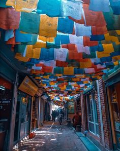 colorful paper hanging from the ceiling in an alleyway with people walking on the sidewalk