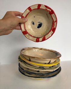 a hand holding a bowl over a stack of plates