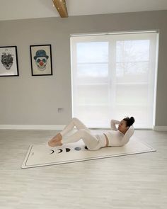 a woman laying on top of a white mat in a room with pictures on the wall