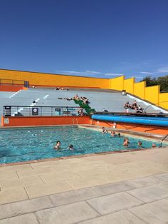 people are swimming in an outdoor pool with yellow and red walls on the sidelines