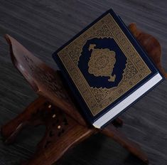 a blue and gold book sitting on top of a wooden chair next to a cross