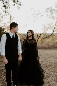 a man and woman dressed in black holding hands while standing next to each other on the ground