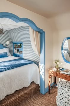 a blue and white bed in a bedroom next to a table with a mirror on it