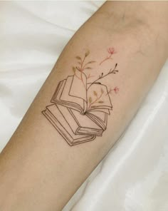 a tattoo on the arm of a woman with an open book and flowers coming out of it