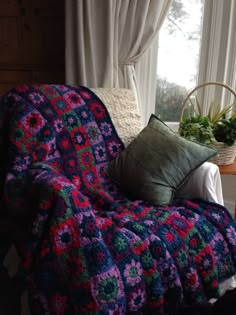 a crocheted blanket sitting on top of a couch next to a pillow and potted plant