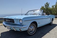 an old blue mustang convertible car parked on the side of the road near the ocean