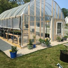 a small greenhouse in the middle of a yard with potted plants on the ground