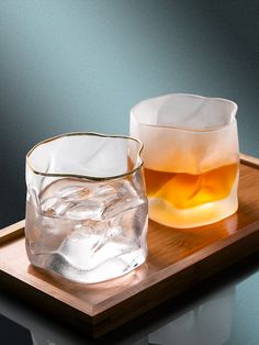 two glasses filled with ice sitting on top of a wooden tray next to each other