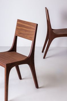 two wooden chairs sitting next to each other on a white surface with one chair facing the camera