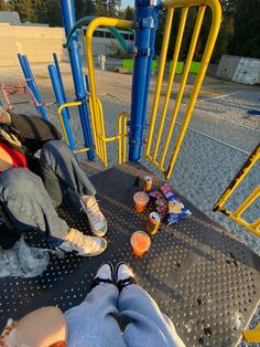 two people sitting on a playground with drinks