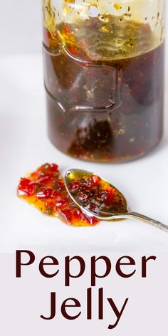 a spoon full of jelly sitting on top of a white table next to a jar