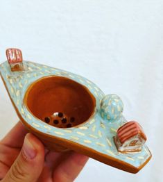 a hand holding a small ceramic object in the shape of a boat