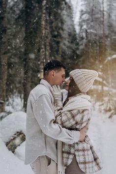 a man and woman are standing in the snow with their arms around each other as they look at each other