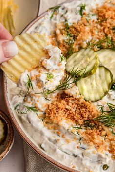 a person dipping crackers into a bowl of dip with cucumbers and dill