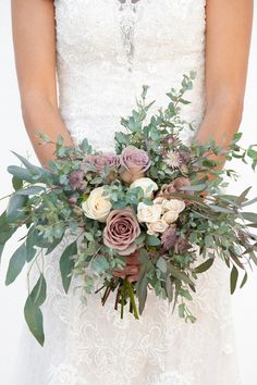 a bride holding a bouquet of flowers and greenery