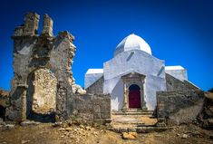 an old white church with a red door in the middle of some rocks and dirt