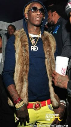 a man in a fur vest and sunglasses standing next to other people at a party