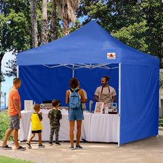 people are standing under a blue tent at the park